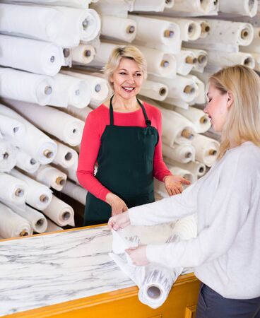 Woman seller is showing fabrics to young buyer in textile shop.の写真素材