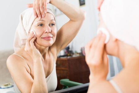 Senior woman starting face cleaning for beauty procedures at homeの写真素材