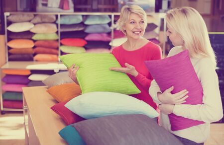 Adult daughter and aged mother choosing pillows in home textile shopの写真素材