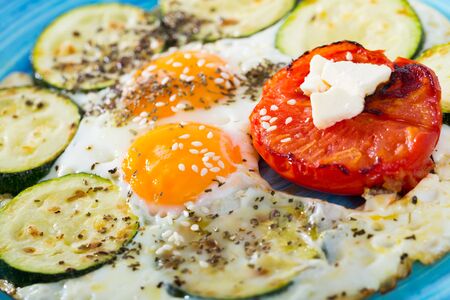 Image of fried eggs with zucchini and tomato on the plate indoors.の写真素材