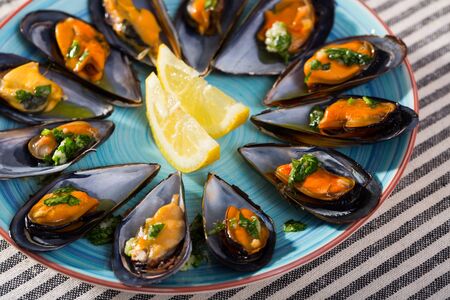 Baked mussels with sauce of oil, garlic and parsley served with lemon slices on color plateの写真素材