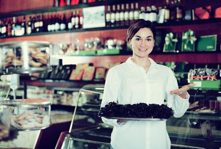 Young female seller offering tray of cakes with icing in confectioneryの写真素材