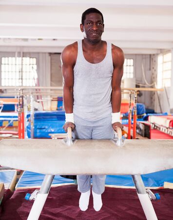 active young afro man in sportswear doing exercises on pommel horse in acrobatic hallの写真素材