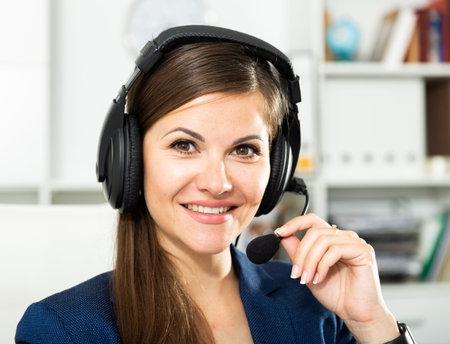 Smiling young female operator talking with customer using headset at company office