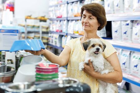 Mature woman visiting pet shop in search of dog bowl for feeding her cute havaneseの写真素材