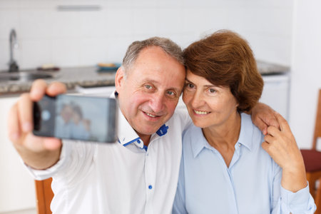 Smiling senior family couple taking selfie on mobile phone at home together