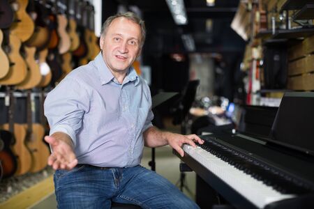 Smiling musician is playing on modern keyboard in music shop.の写真素材