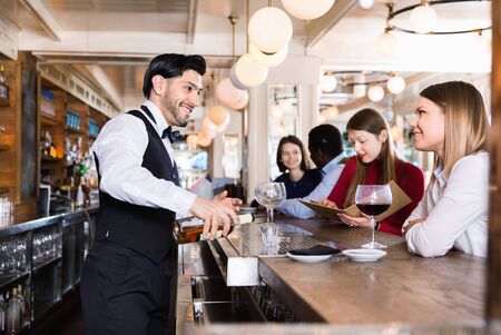 Cheerful positive  barman is servicing young people who are relaxing in bar indoor.の写真素材