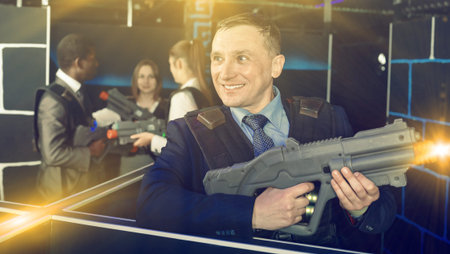 Man in business suit holding the laser gun and playing laser tag with colleagues