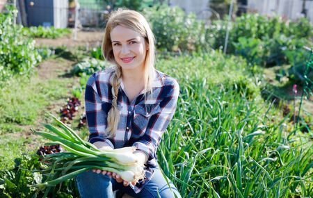 Smiling young woman gardener holding green onion  in garden outdoorの写真素材
