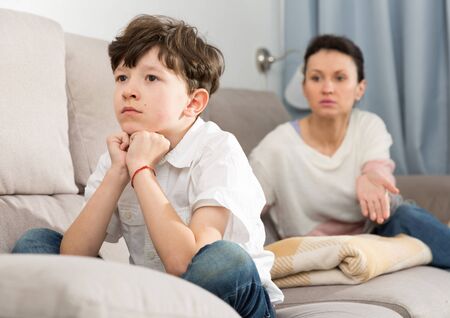 Frowning tweenager listening to reprimanding from his mother at homeの写真素材