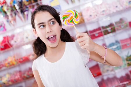 Portrait of attractive emotional  schoolgirl standing with lollipop on stick in  storeの写真素材