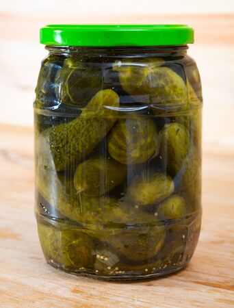 Glass jar with pickled cucumbers on a wooden tableの写真素材