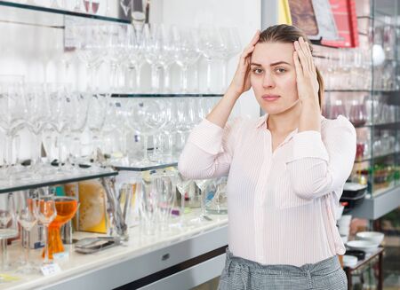 Adult worried female customer choosing wineglass in the tableware storeの写真素材