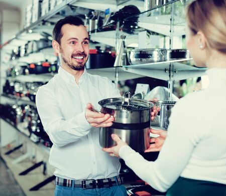 Young male salesman shows the assortment of saucepans in the storeの写真素材