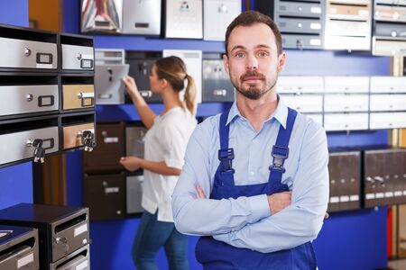 Confident salesman in blue overall standing in mailbox storeの写真素材