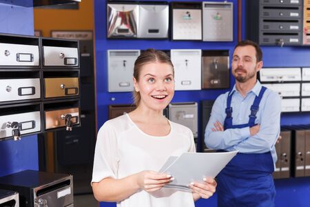 Young woman choosing postbox in shop, asking for information from male sellerの写真素材
