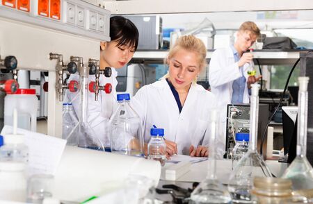 Two girls students of Faculty of Chemistry performing experiments in university laboratory, recording results in workbookの写真素材