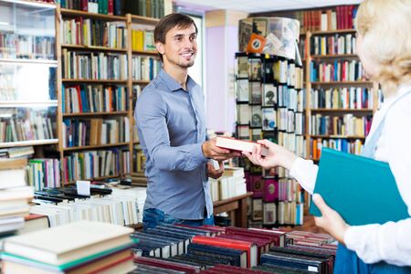 Young cheerful man taking new book from seller in book storeの写真素材