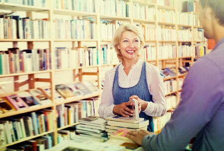 Cheerful woman taking book in book shop and talking to sellerの写真素材