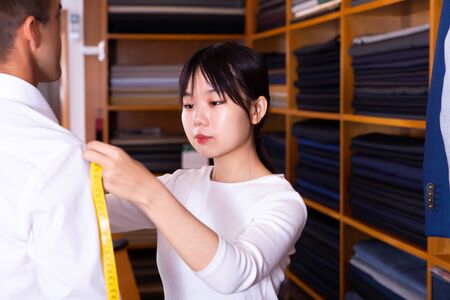 Woman tailor makes measurements of customer clothes in shopの写真素材