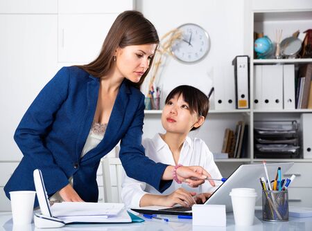 Portrait of two successful businesswomen confidently working on laptop in modern officeの写真素材
