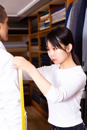 Chinese female shop assistant measuring male client for selecting suit coat in men clothing storeの写真素材