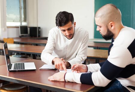 Portrait of two young guys working on their student project at desk in classroomの写真素材