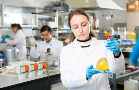 Professional female chemist working in laboratory, analyzing liquid samples in test flasks