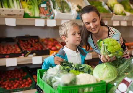 Portrait of happy woman and her little son choosing vegetables at shopの写真素材