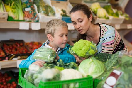 Portrait of happy woman and her little son choosing vegetables at shopの写真素材