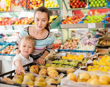 Positive smiling mother with little boy buying pears and apples at storeの写真素材