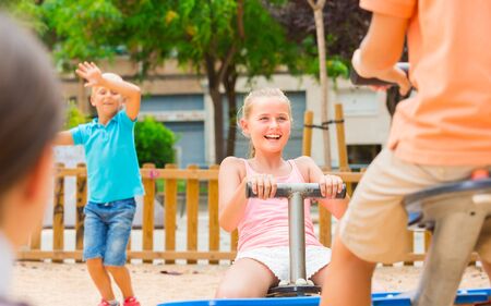 Cheerful children are teetering on the swing on the playground.の写真素材