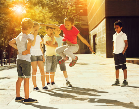 Energetic kids playing and skipping on elastic jumping rope in european yard