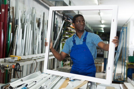 Male master is working with window frame in the window workshop.