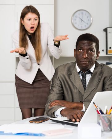 Angry woman boss pointinting to misses in work to man manager working at table with  laptopの写真素材