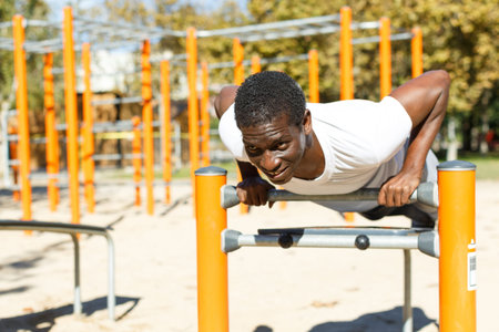 Athletic african  american male performs warm-up exercises at chin-up bar in park