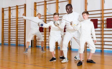 Fencing instructor explaining to young fencers effective movements and techniques in a training roomの写真素材