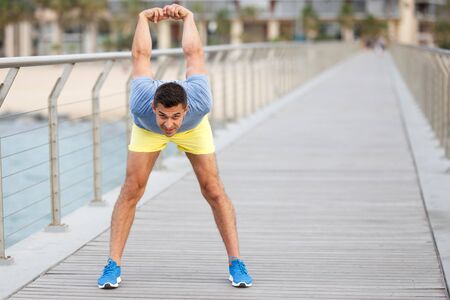 Positive male doing exercises on pier during morning workoutの写真素材