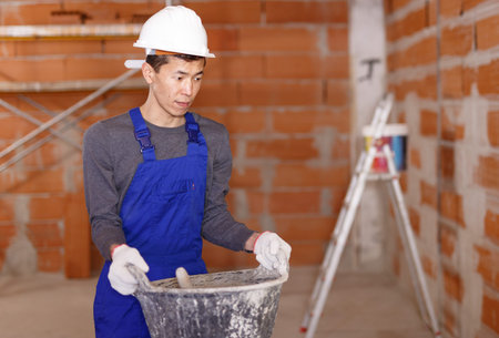 Portrait of Asian builder in process of finishing work in cottage