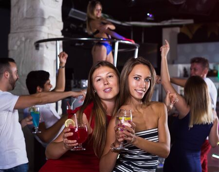 Cheerful females friends with cocktail dancing in night club on partyの写真素材
