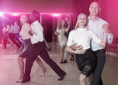 Smiling adult pairs practicing salsa movements in modern dance studio