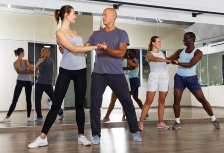 Young smiling people practicing vigorous jive movements in dance studio