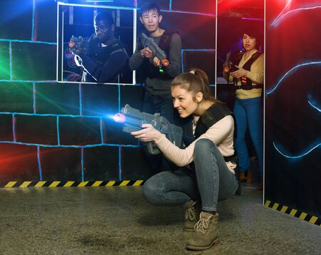 Emotional young girl with laser pistol playing laser tag with multinational team on dark labyrinthの写真素材