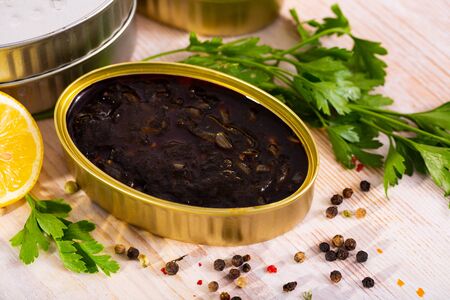 Canned seafood, chopped squid in ink served on wooden table with parsley and pepperの写真素材