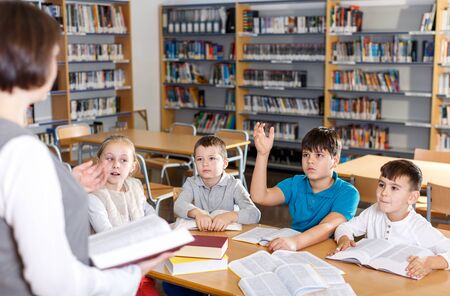 Group of school kids studying in school library with friendly female teacher