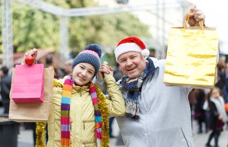 Happy friendly family of father and teen daughter holding bags after shopping on Christmas marketの写真素材