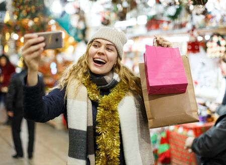 Portrait of beautiful girl taking selfie on her smartphone at Christmas fairの写真素材