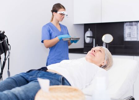 Mature female client lying on sofa waiting for cosmetological treatment in professional  aesthetic clinicの写真素材