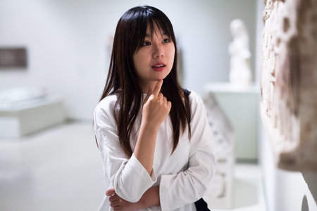 Young chinese woman visitor  looking at exhibition in museum of ancient sculptureの写真素材